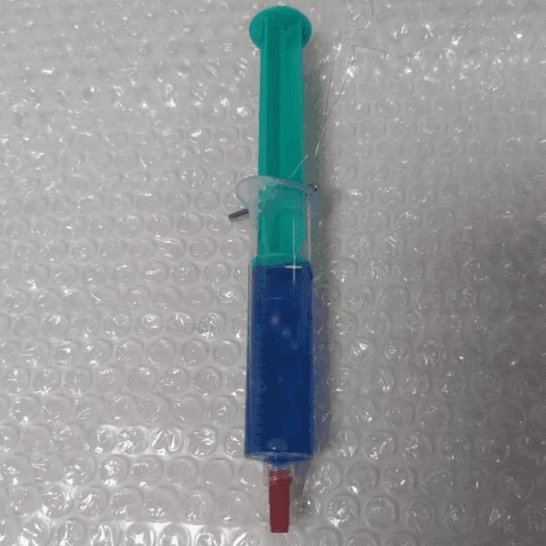 A syringe filled with blue dye showing dye ingress through a deliberate flaw, used as a positive control in rotational dye ingress testing.