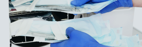 Paper-film sterilisation pouches containing medical instruments being loaded into an autoclave by a gloved operator