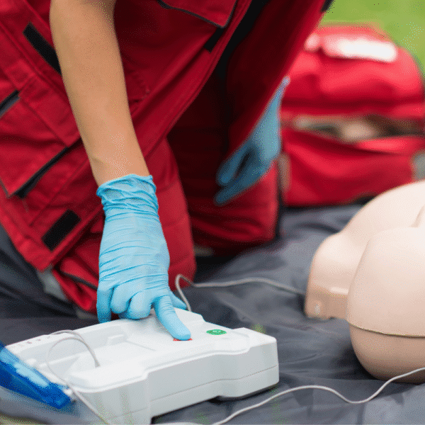 Close-up of a responder activating an automated external defibrillator during emergency resuscitation, representing AED performance and reliability testing.