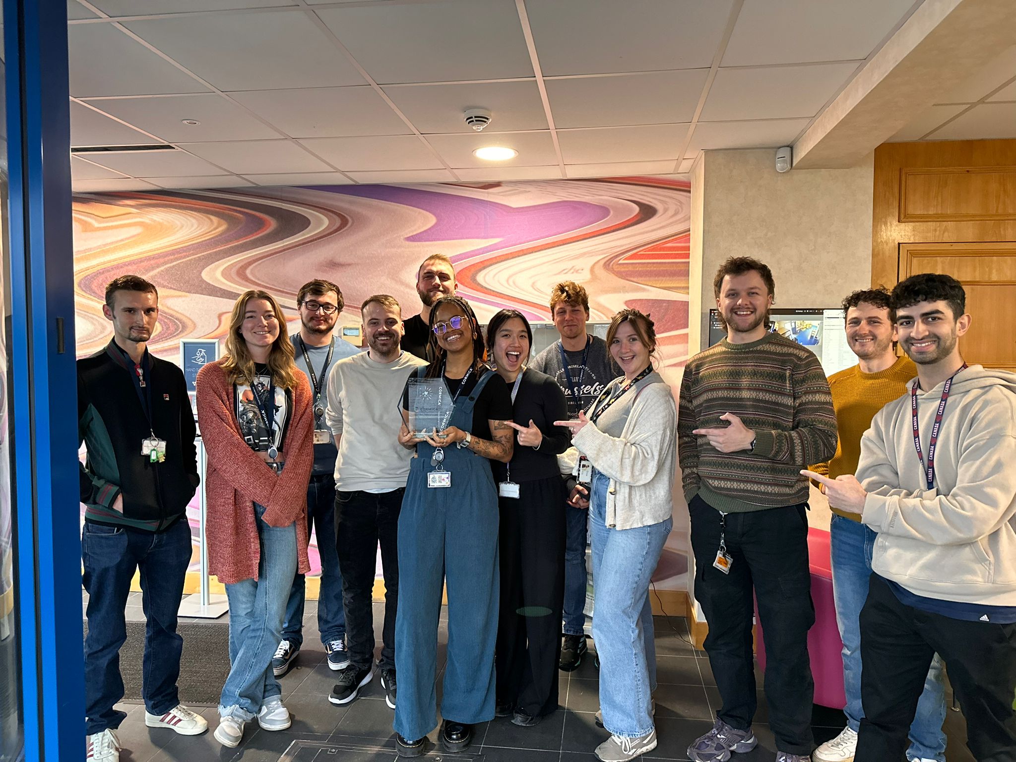 Cormica Wickham team celebrating indoors while holding a Global Health & Pharma award recognising excellence in pharmaceutical and medical device testing.
