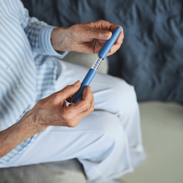 Close-up photograph of an older adult holding an injection pen device with a visible dose window.