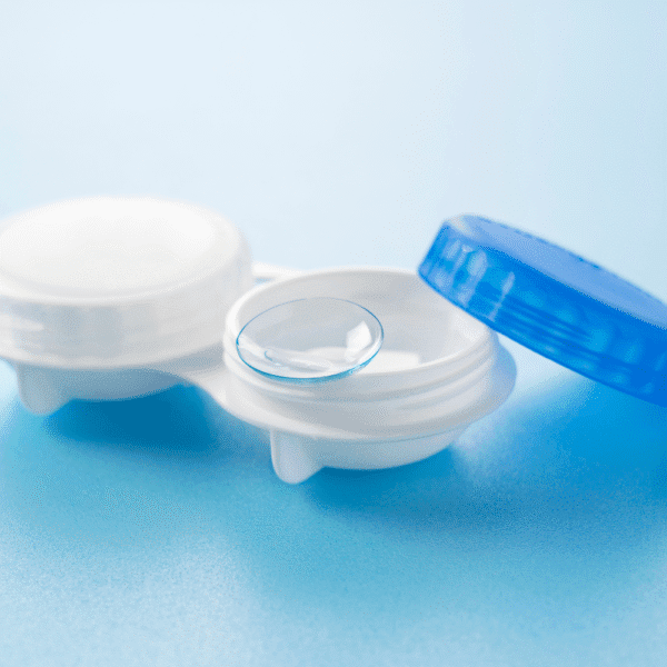 Close-up studio image of a soft contact lens placed in an open contact lens storage case on a blue background.