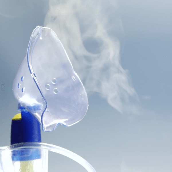 Close-up photograph of a nebuliser mask releasing mist, illustrating aerosol drug delivery for respiratory therapy.
