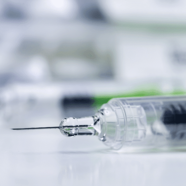 Macro photograph of a pre-filled syringe showing the needle, glass barrel and plunger stopper on a clean clinical surface.