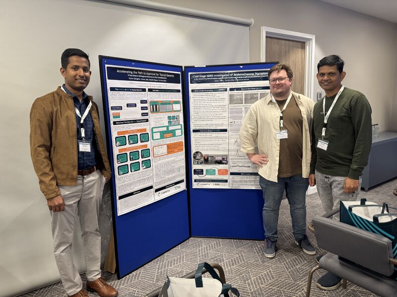 Cormica's conference attendees stand beside a large double-sided scientific poster display at an industry event. The posters present research on topical generic drug development and cold-stage MDRS investigations.