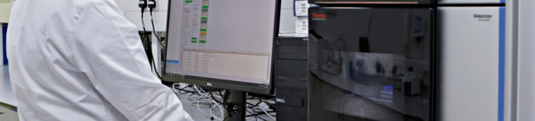 Scientist operating an HPLC-UPLC analytical chromatography system in a laboratory, monitoring sample data on screen as part of pharmaceutical and medical device testing.